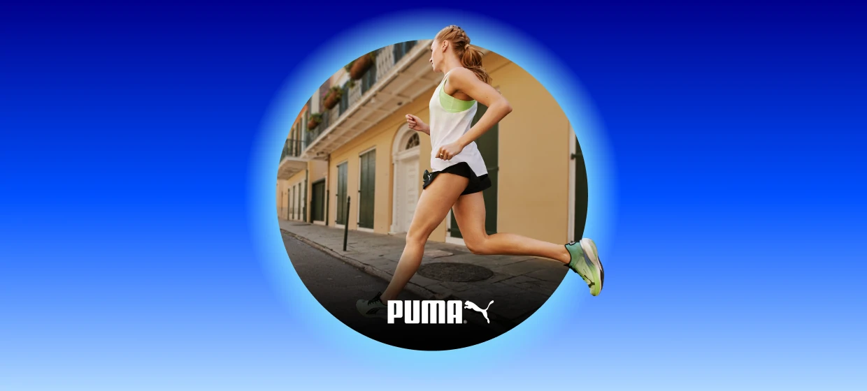  Seitlich laufende Person in weißem Sporttop, schwarzer Shorts und grünen Laufschuhen auf einer Stadtstraße; unten das Puma-Logo. 