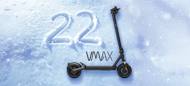  Seitenansicht des VMAX VX2 HUB E-Scooters vor verschneitem Hintergrund. Links davon die in den Schnee geschriebene Zahl 22. Über dem Trittbrett des E-Scooters das VMAX-Logo. 