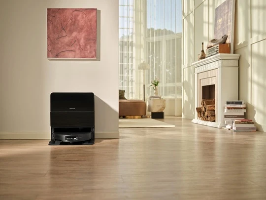  Schwarzer Roborock Saros 10 Saug- und Wischroboter in seiner Ladestation in einem hellen, modernen Wohnzimmer mit Holzboden, Kamin und großer Fensterfront. 