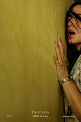 Das Filmplakat zeigt eine angespannte Frau, die sich dicht an eine gelblich-grüne Wand drückt. Ihr Gesicht ist nur teilweise sichtbar, da sie am rechten Bildrand angeschnitten ist. Dunkle Haarsträhnen fallen ihr ins Gesicht, ihr Mund ist leicht geöffnet, und ihre Hand liegt flach an der Wand. Dadurch entsteht der Eindruck, als würde sie lauschen, sich verstecken oder vorsichtig durch einen engen Raum bewegen.