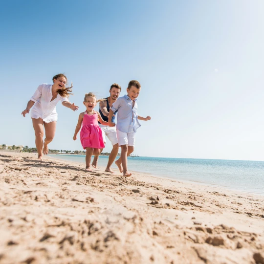  Familie läuft lächelnd an einem sonnigen Tag einen Nordsee-Strand entlang 