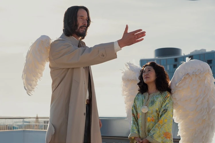  Keanu Reeves in seiner Rolle als Gabriel. Er trägt Engelsflügel und zeigt mit seinem Arm auf etwas. Sandra Oh trägt in ihrer Filmrolle ebenfalls Engelsflügel und sieht ihn aufmerksam an. Im Hintergrund sind Gebäude zu erkennen. 
