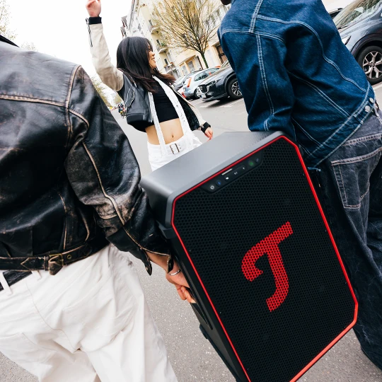 Gewinnspiel Teufel Drei Personen laufen draußen auf der Straße. Eine Person trägt einen Party-Lautsprecher von Teufel.