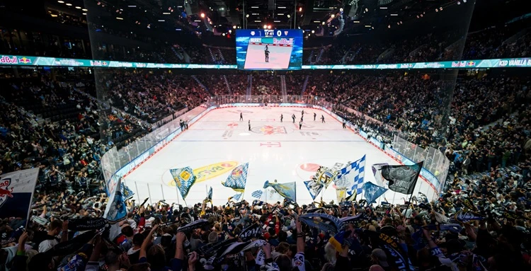 Gewinnspiel EHC Volles Eishockey-Stadion mit jubelnden Fans, die Fahnen und Schals schwenken, während auf dem Eis ein Spiel läuft