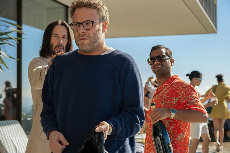  Seth Rogen, Keanu Reeves und Aziz Ansari in ihrer jeweiligen Filmrolle. Keanu Reeves hat die Hand auf die Schulter von Seth Rogen gelegt. Dieser hat einen erschrockenen Blick. Die Personen befinden sich draußen auf einer Terrasse. 