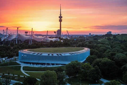 Gewinnspiel EHC SAP Garden im Münchner Olympiapark bei Sonnenuntergang mit Olympiaturm und Zeltdachkonstruktion im Hintergrund.