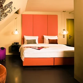  Helles Hotelzimmer mit Doppelbett, Sessel und Wanddekoration. 