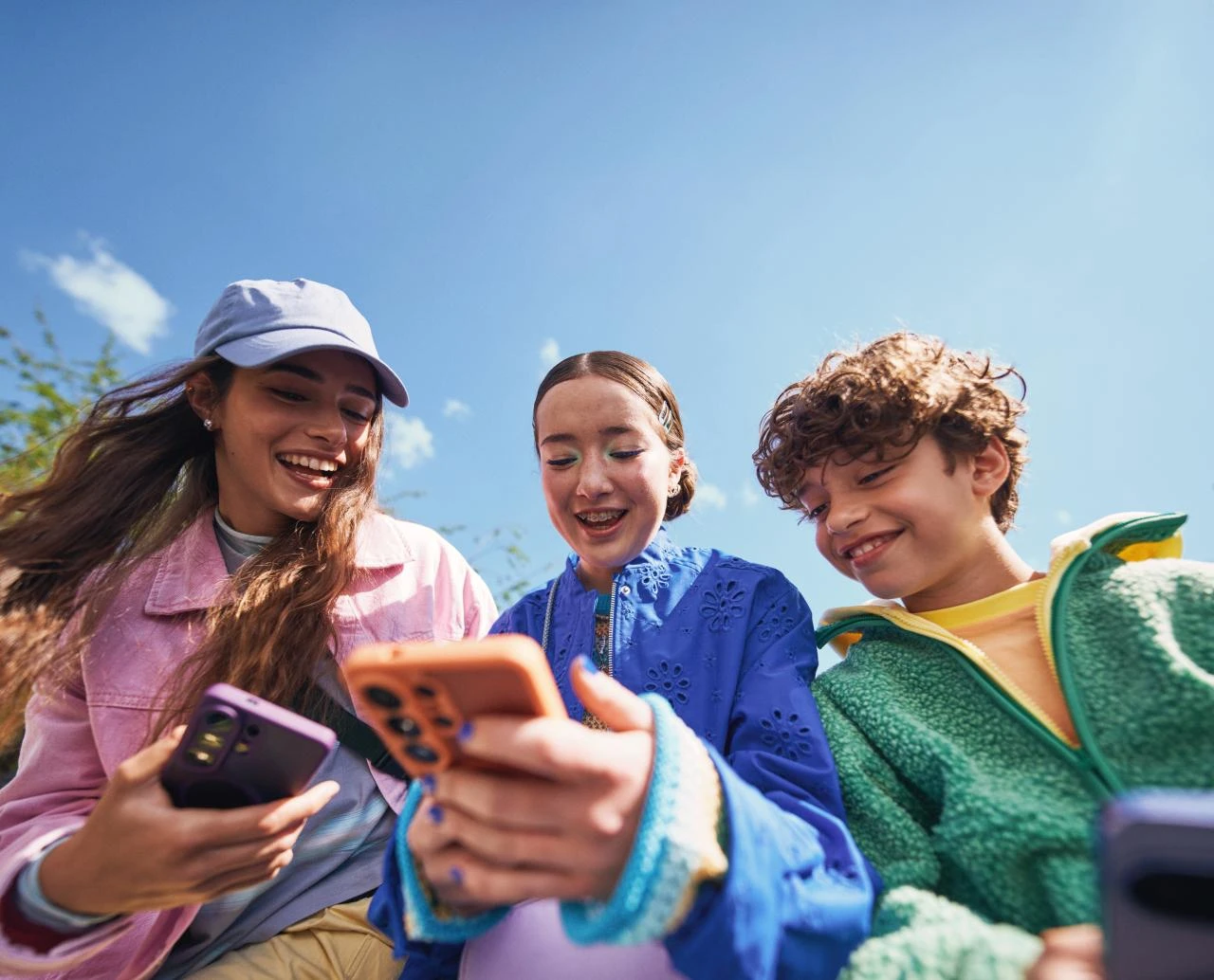  Drei Jugendliche im Freien betrachten gemeinsam ihre Smartphones.
