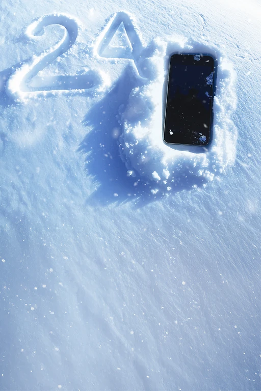  Ein Smartphone, welches zum Teil mit Schneeflocken bedeckt ist, liegt im Schnee. Links daneben die Zahl 24 in den Schnee geschrieben. 