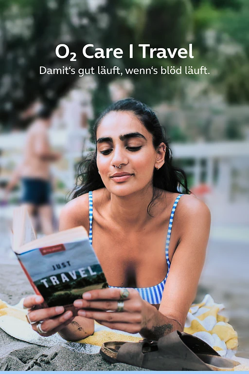  Eine Frau liest ein entspannt ein Buch am Strand. 