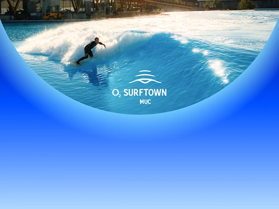  Surfer reitet bei strahlendem Sonnenschein eine künstliche Welle, im Wasser ist das Logo von O2 Surftown MUC zu sehen
